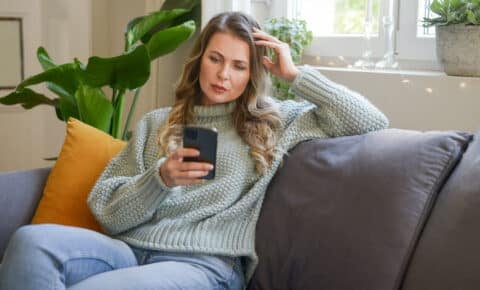 Eine Frau sitzt auf dem Sofa und schaut auf ihr Smartphone